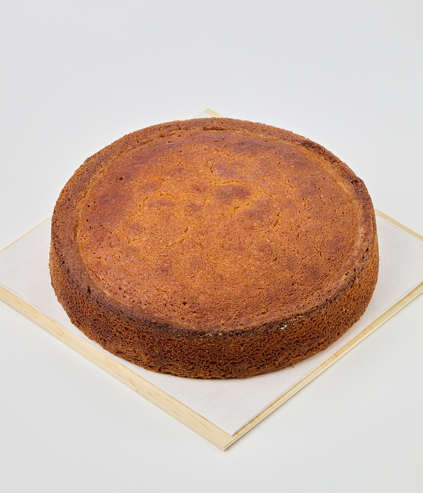 A whole round golden-brown almond cake resting on parchment paper atop a wooden gift box filled with pale wood shavings.