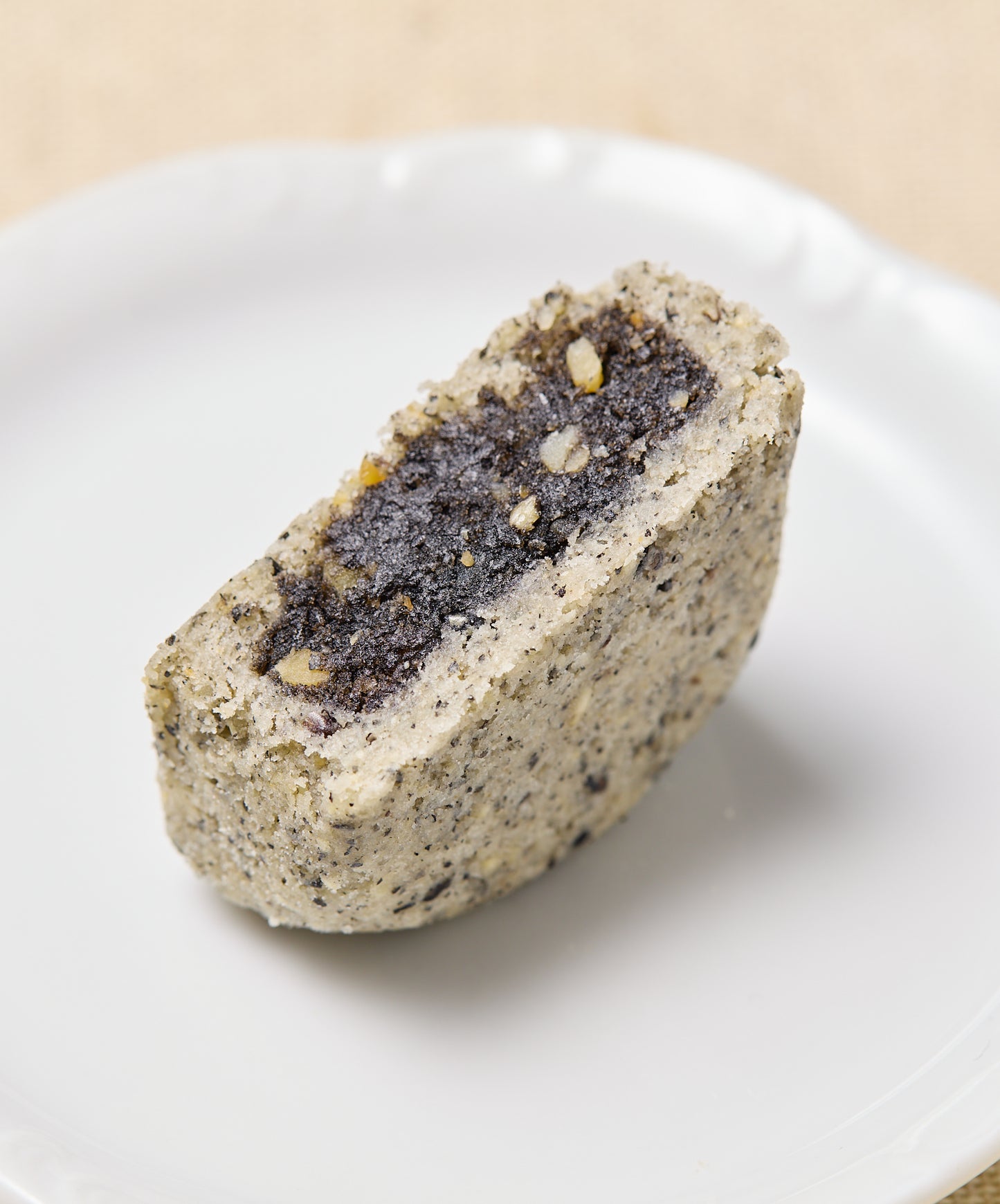A cross-section of the black sesame cake reveals a dense, dark black sesame filling with visible nut pieces inside a lighter speckled crust.