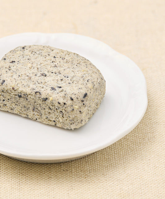 A side view of the black sesame cake, showing its textured, speckled gray exterior on a white plate.