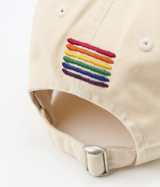 Back of the cream cap showing six embroidered rainbow stripes above the adjustable metal buckle closure