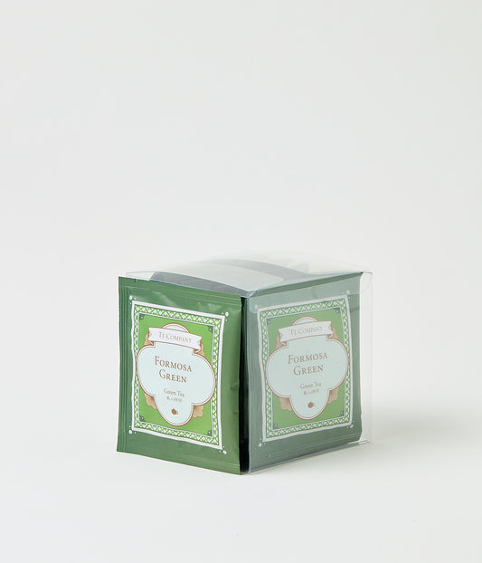 Stack of Te Company Formosa Green green tea packets packaged in a clear plastic box against a white background.