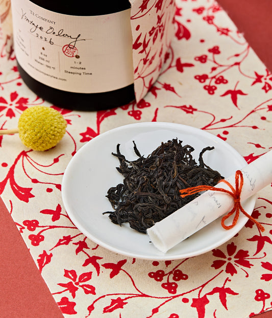 Tea leaves on a white plate with decorative items on a floral paper.