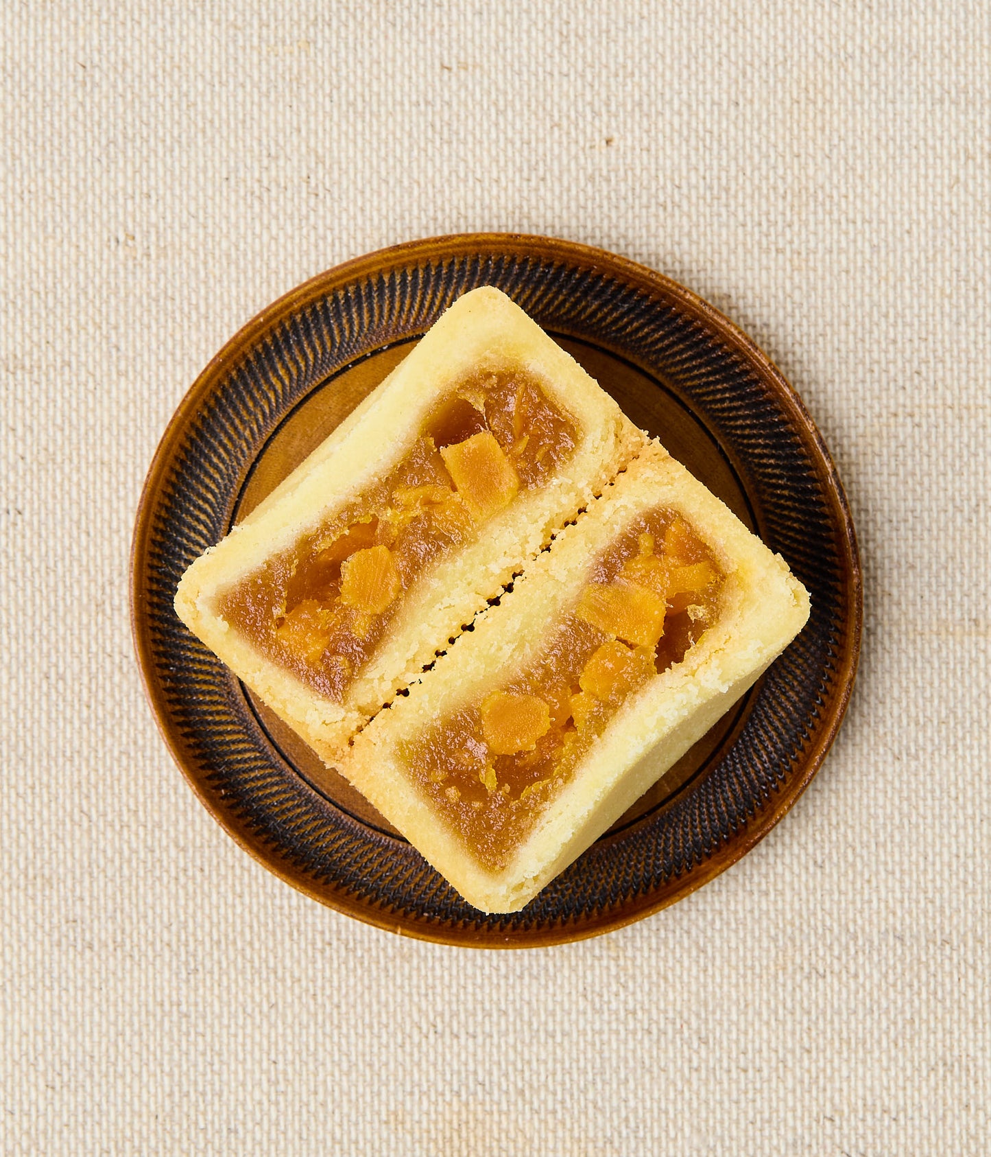 Cross-section of a Taiwanese pineapple cake showing salted egg yolk filling on a brown patterned plate.