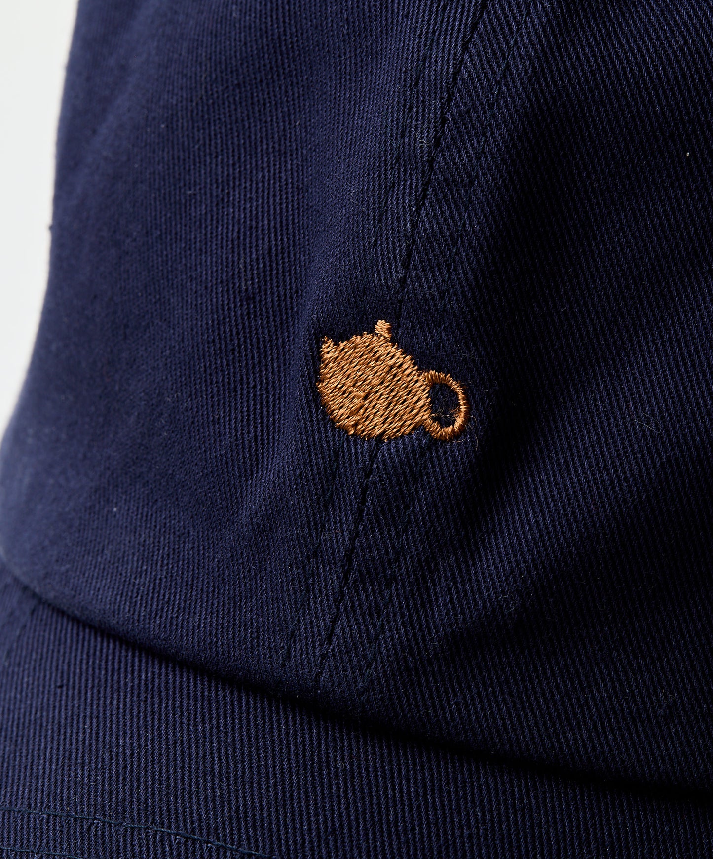 Close-up of golden embroidered teapot design on navy blue fabric.