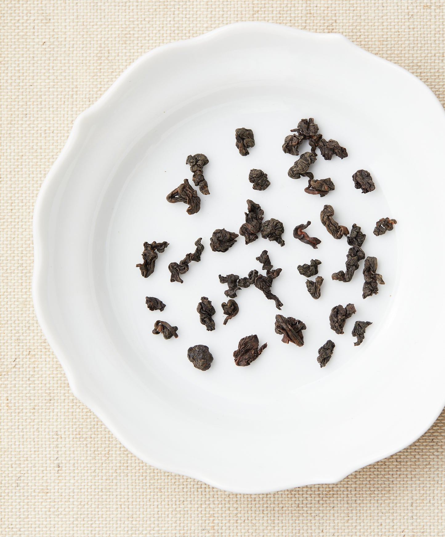 Dry Iron Goddess Archetype oolong tea leaves scattered on a white plate.
