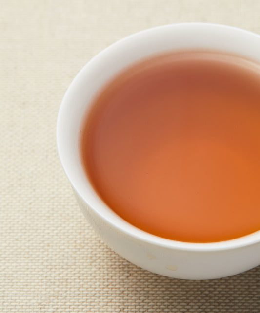 A cup of amber-colored Iron Goddess Archetype tea on a textured surface