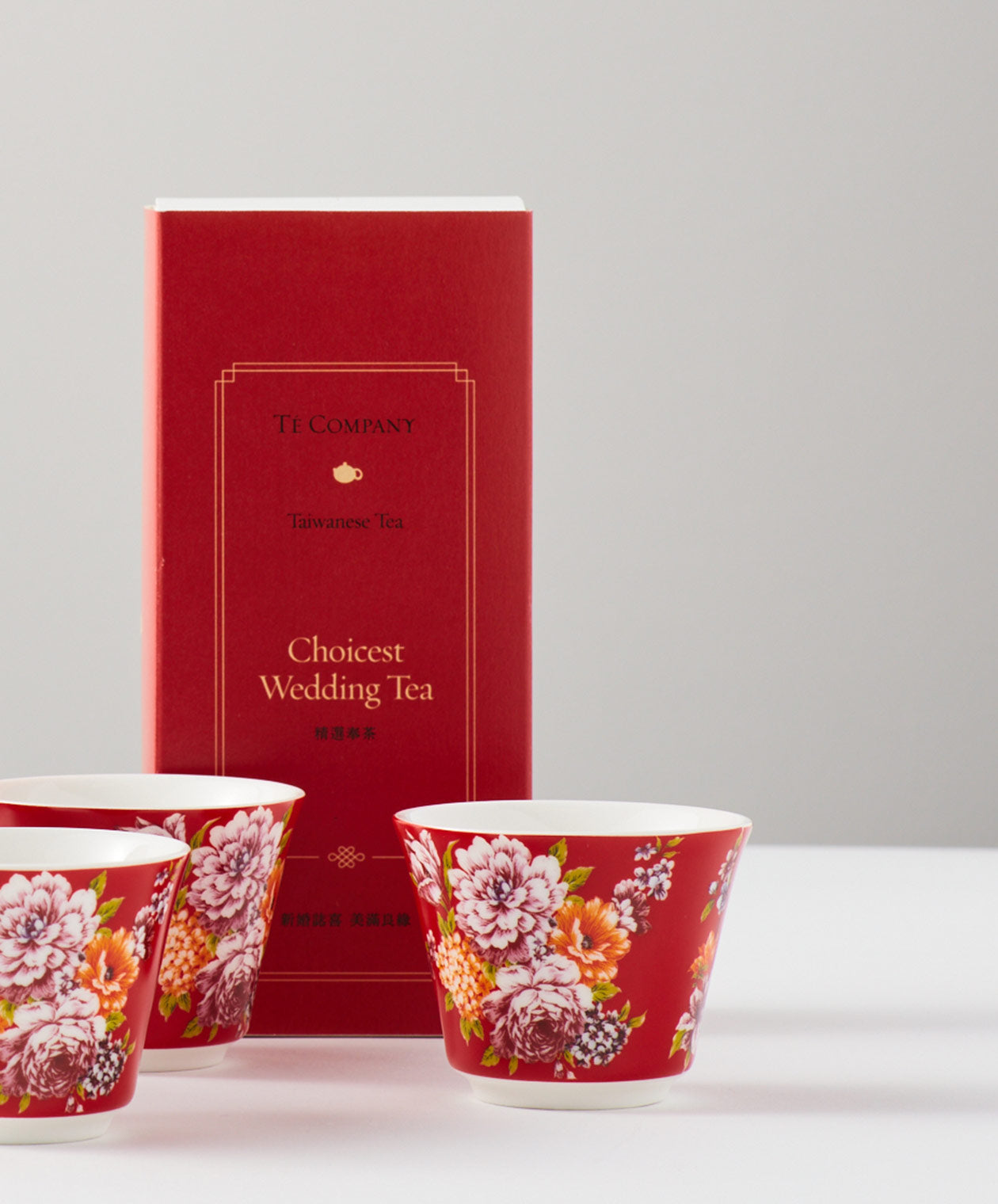 Three red floral tea cups placed in front of a red box labeled ‘Choicest Wedding Tea’ by Té Company.