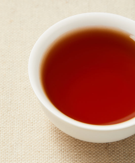 A close-up of reddish-brown tea in a white teacup placed on a beige textured background.