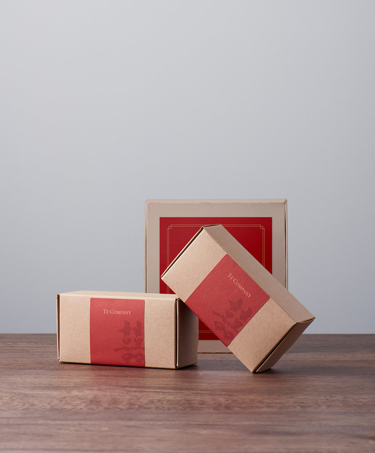 Two brown gift boxes with red labels from Té Company next to a larger box.
