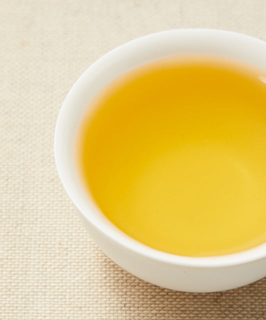 A close-up of a white teacup filled with golden-yellow tea on a beige textured background.