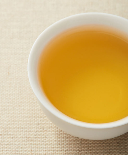 A close-up of a white teacup filled with golden-yellow tea on a beige textured background.