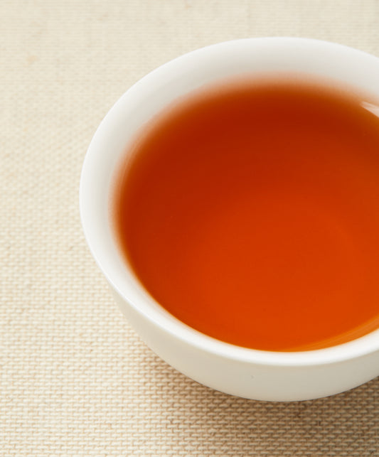 A close-up of reddish-brown tea in a white teacup placed on a beige textured background.