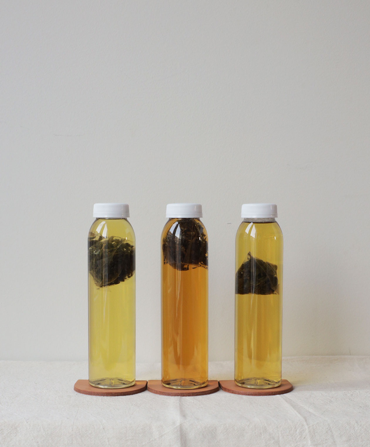Three clear bottles of cold brew tea, each containing a tea sachet, with varying shades of golden tea on a white surface.