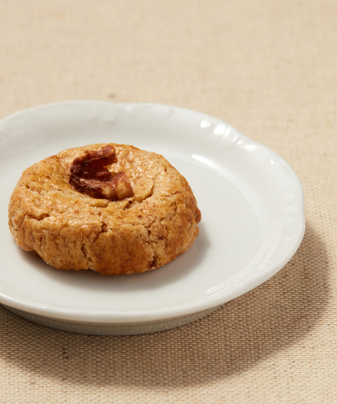 Close-up of a walnut-topped Button Cookie on a white plate