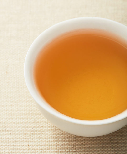 A cup of golden White Peony tea on a textured surface.