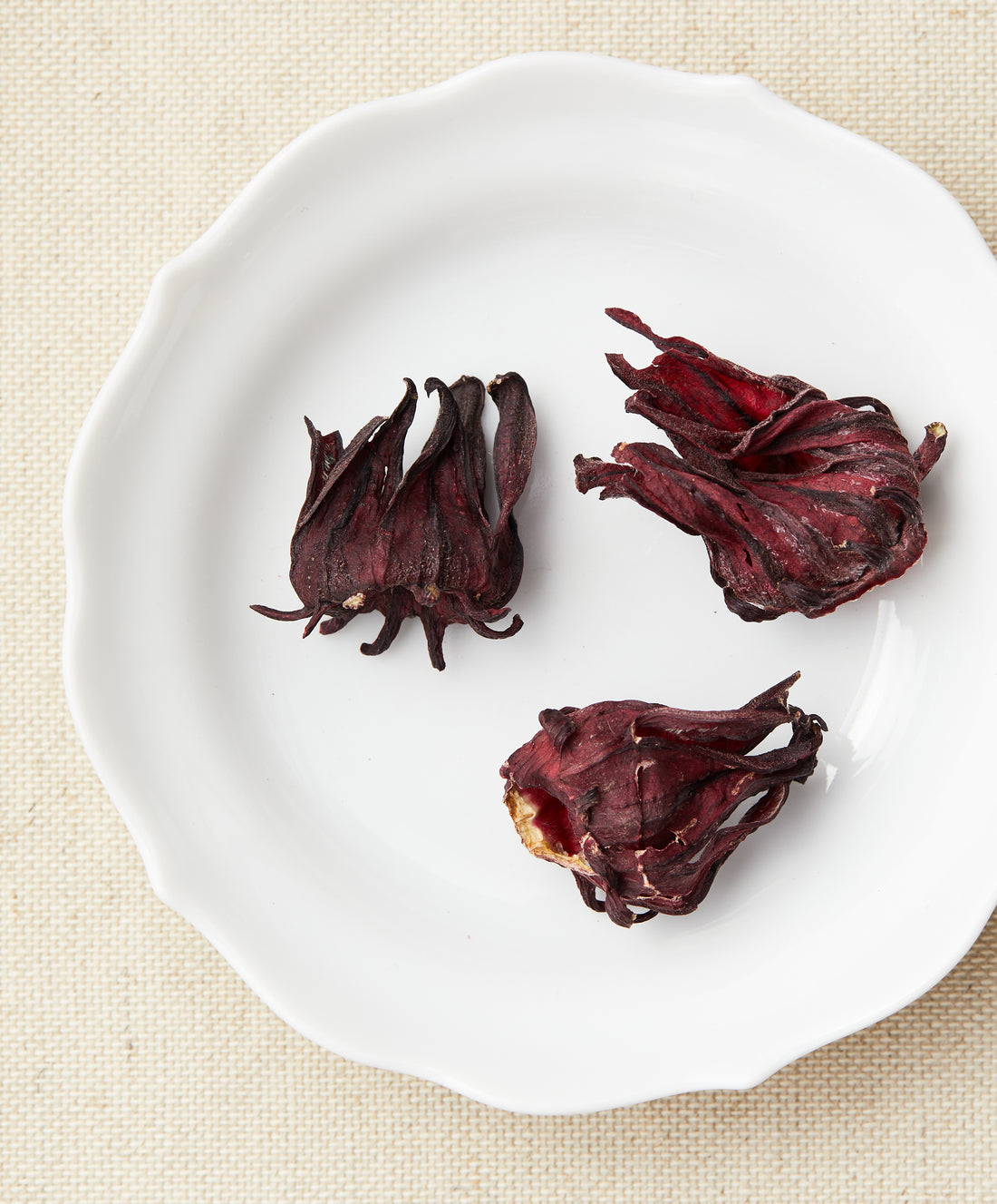 Three dried hibiscus flowers on a white plate.