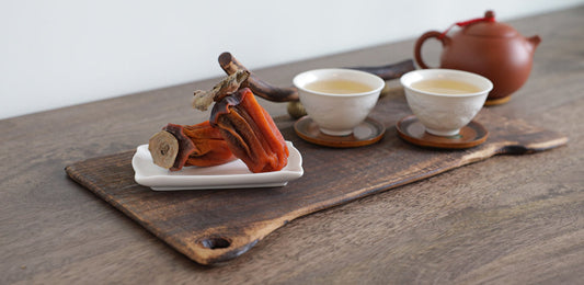Dried persimmons with tea set on wooden board.