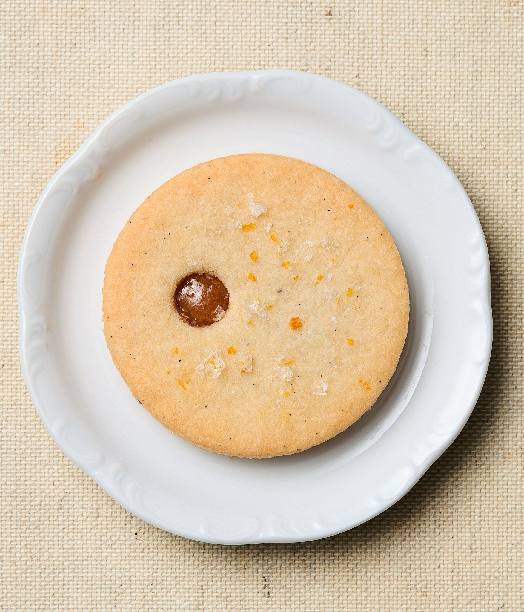 linzer cookie with a calamansi center on a white plate against a beige background