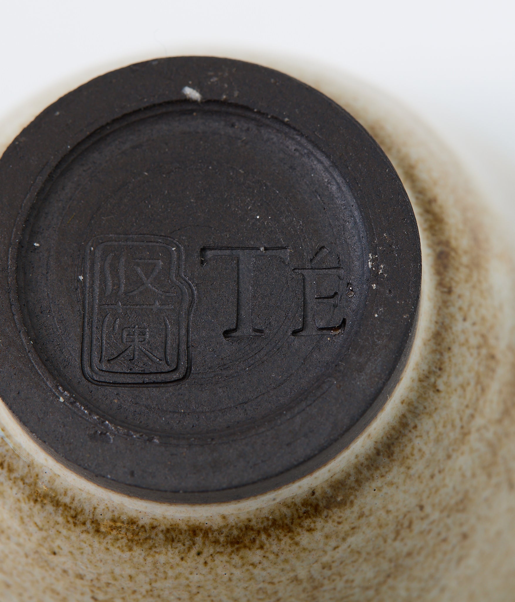 Close-up of a ceramic product with a black circular mark and text on a beige background