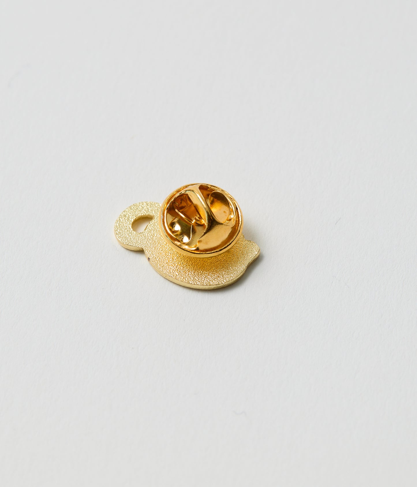 Gold-colored lapel pin on a light gray background