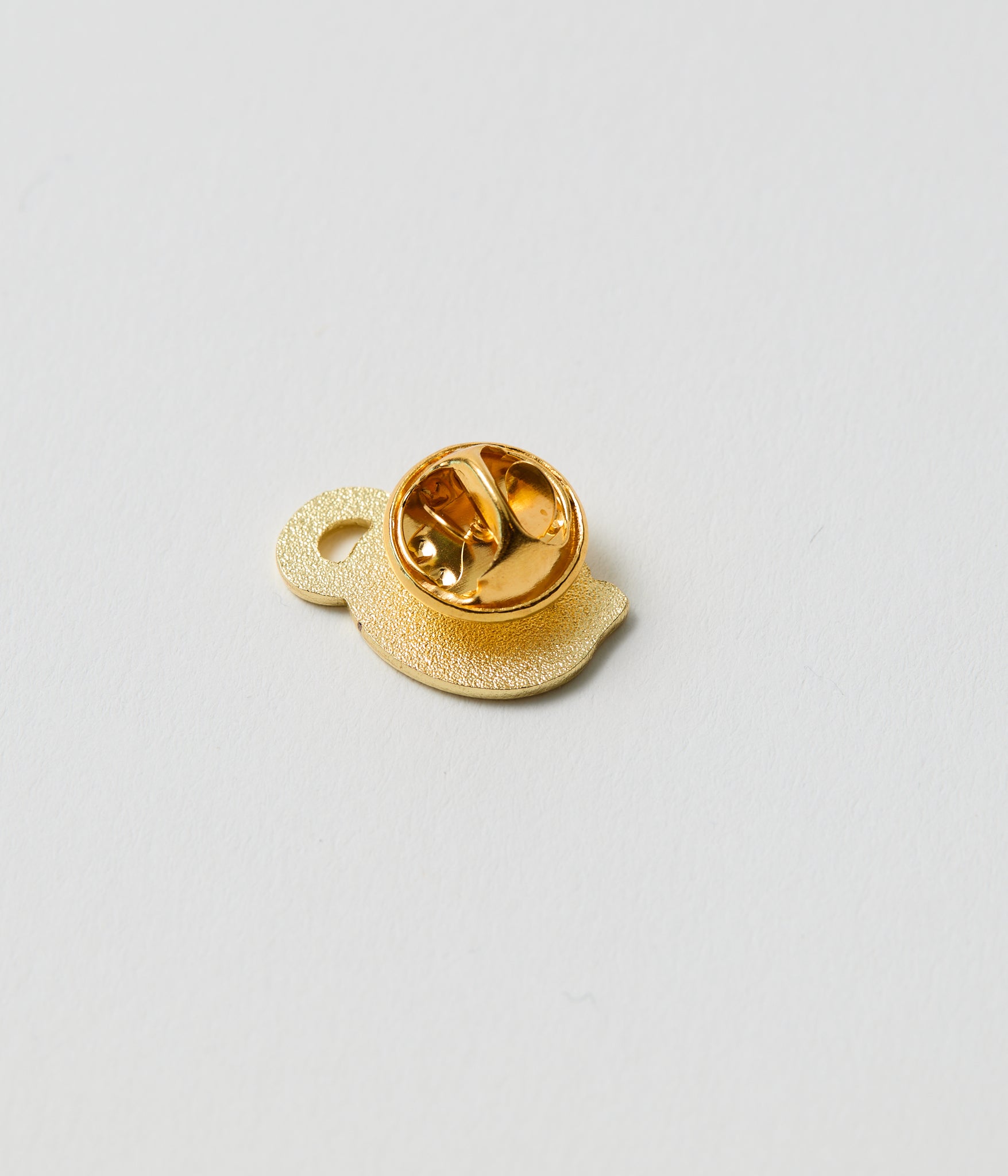 Gold-colored lapel pin on a light gray background