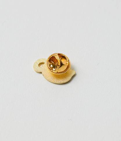 Gold-colored lapel pin on a light gray background