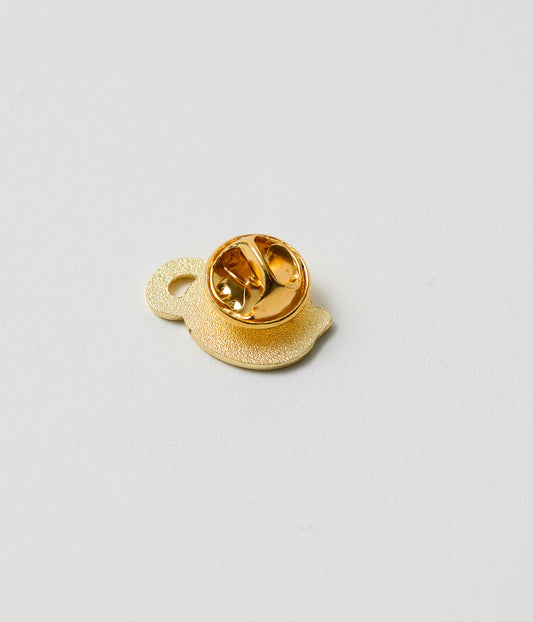 Gold-colored lapel pin on a light gray background