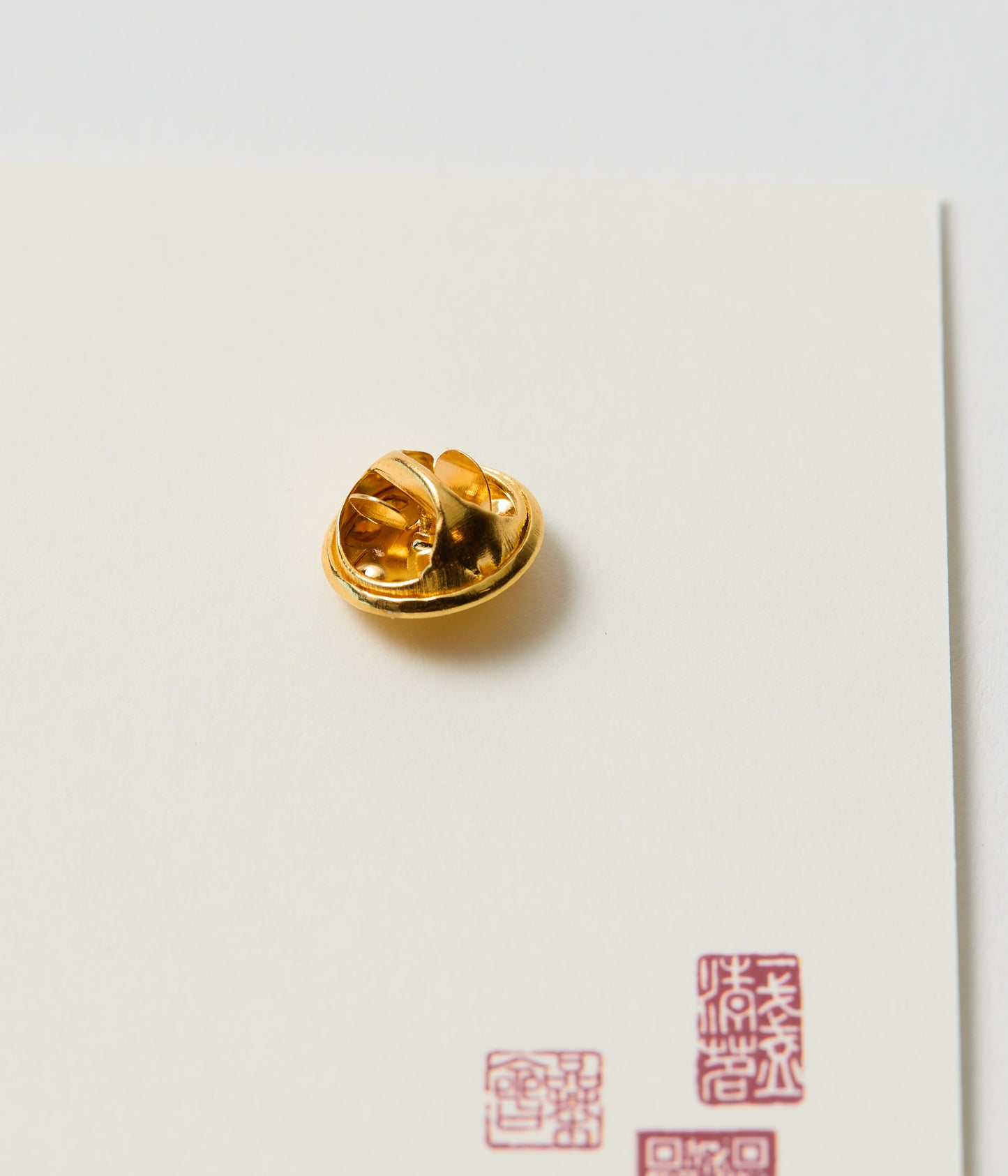 Gold lapel pin back on a white card with red text