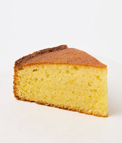 A single slice of almond cake showing a moist, pale-yellow crumb and a deep golden-brown crust along the top edge.