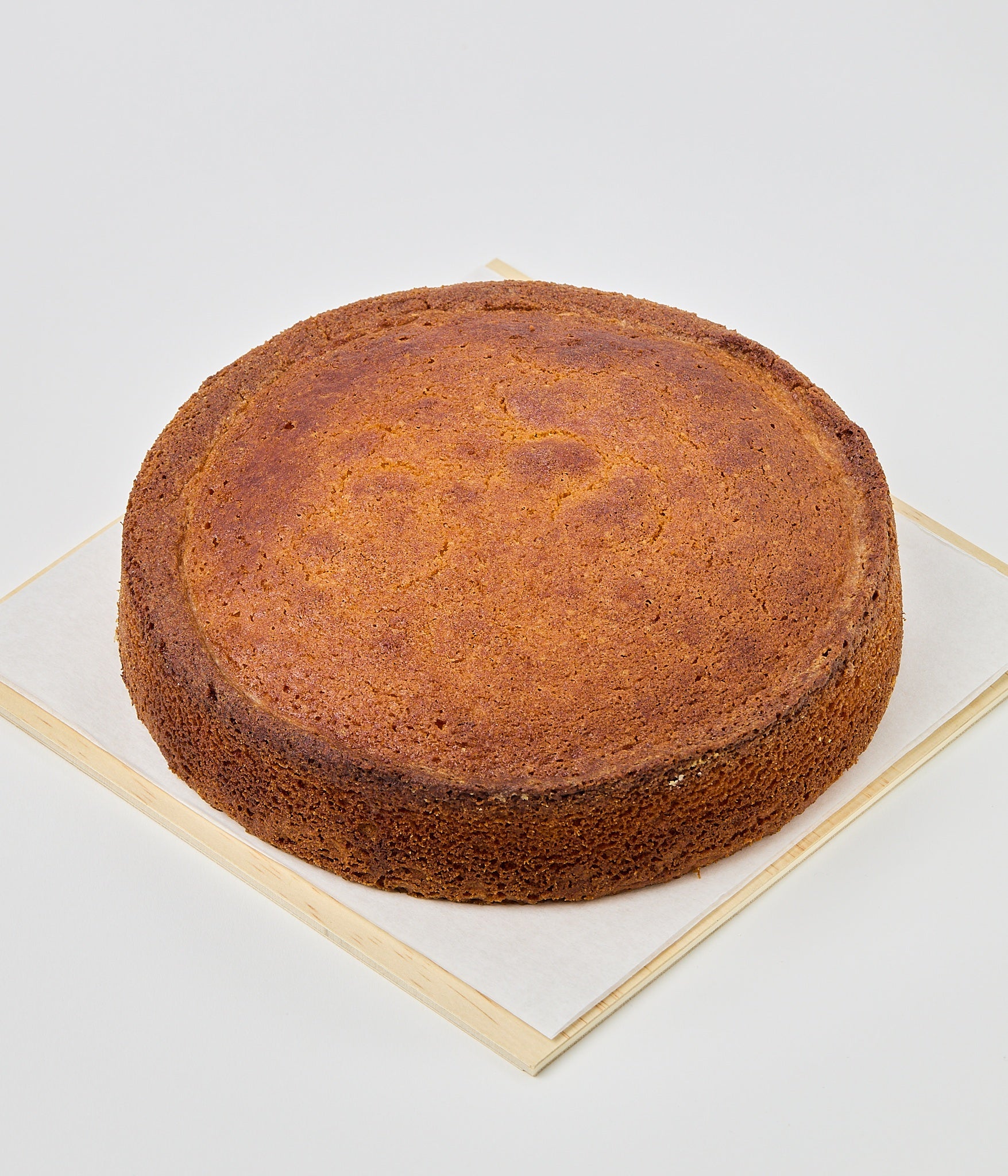 A whole round golden-brown almond cake resting on parchment paper atop a wooden gift box filled with pale wood shavings.