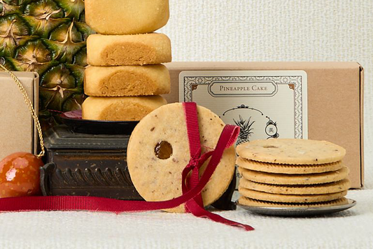 Assorted cookies with a pineapple cake box and decorative ribbons on a textured surface.