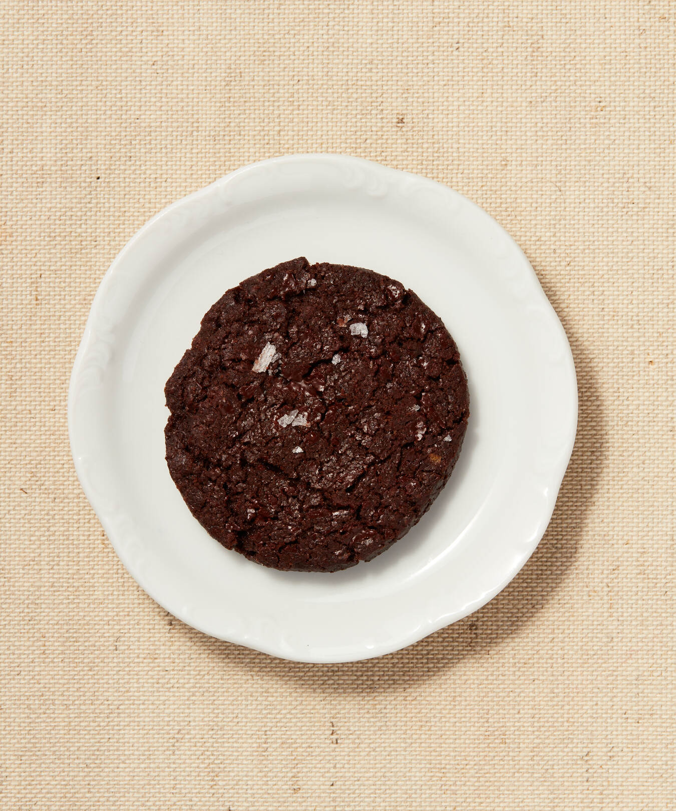 Single chocolate Button Cookie with sea salt on a white plate.