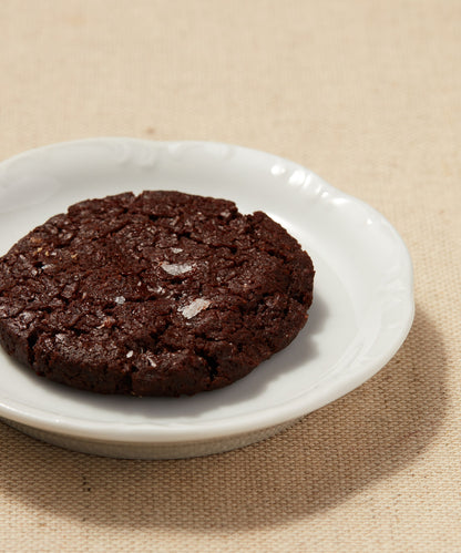 Close-up of a chocolate Button Cookie with sea salt on a white plate.