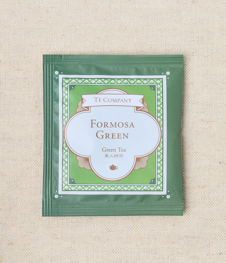 Single packet of Te Company Formosa Green green tea on a beige textured background.