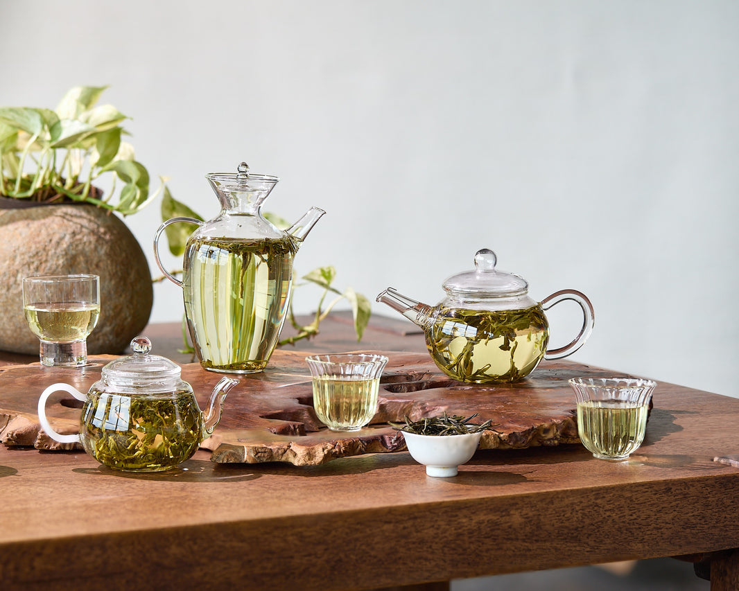 Tea-making setup with glass teapots and cups on a wooden table.