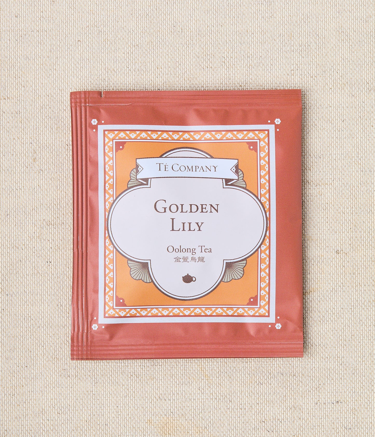 Single packet of Te Company Golden Lily oolong tea on a beige textured background.