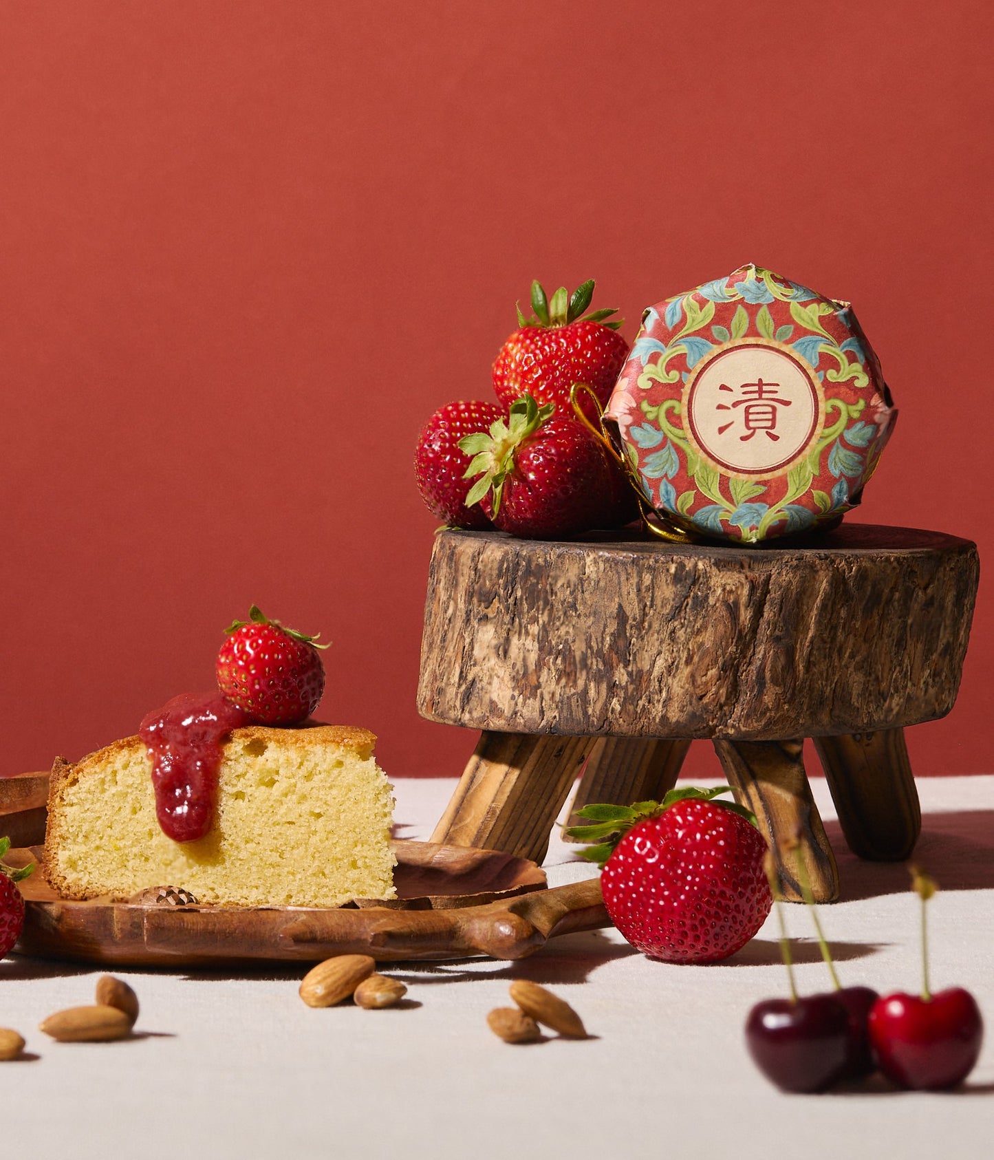Slice of cake with strawberry sauce, strawberries, and a decorative box on a wooden stand against a red background.