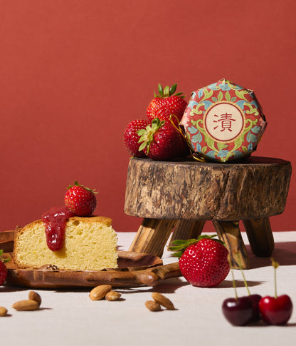 Slice of cake with strawberry sauce, strawberries, and a decorative box on a wooden stand against a red background.