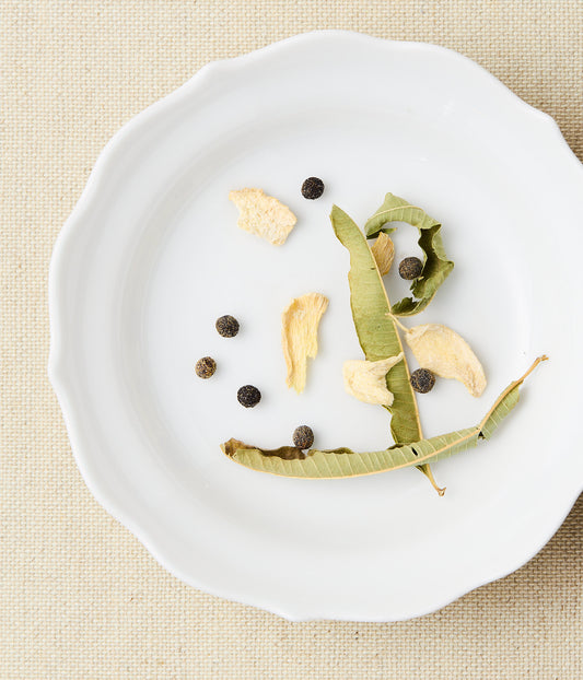 Dried leaves, ginger, and maqaw peppercorns on a white plate.