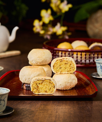 Traditional Chinese pastries on a wooden tray with a teapot and cups in the background.