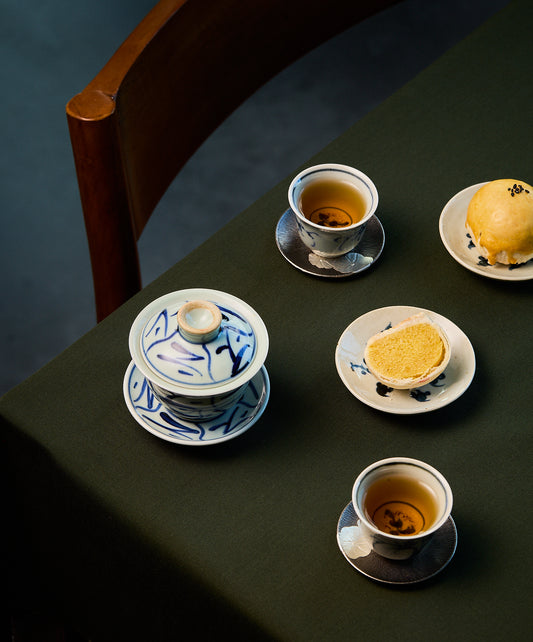 Tea cups and mooncakes on a dark surface with a wooden chair.