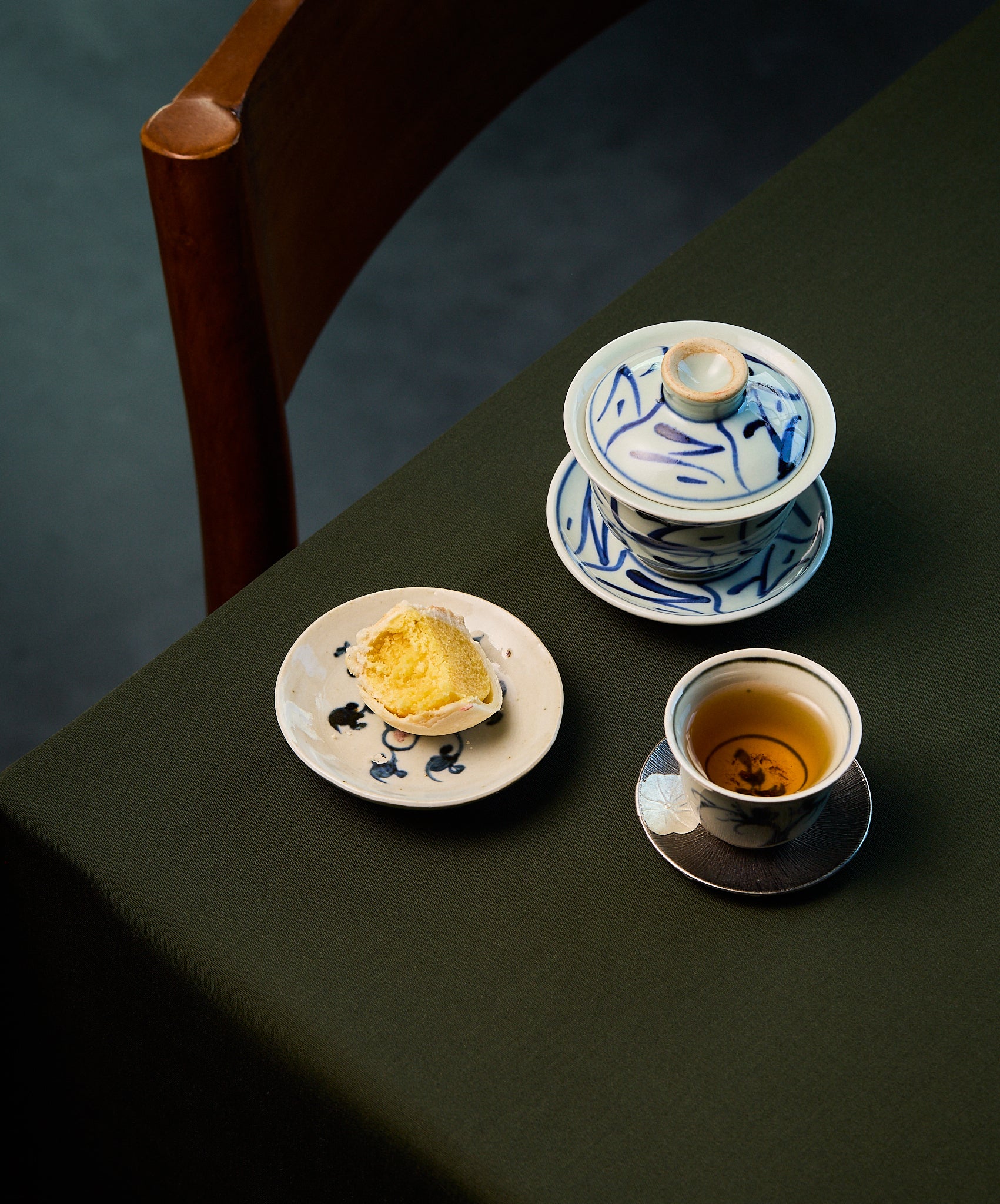 Tea set with a teapot, cup, and half eaten mooncake on a plate on a dark surface.