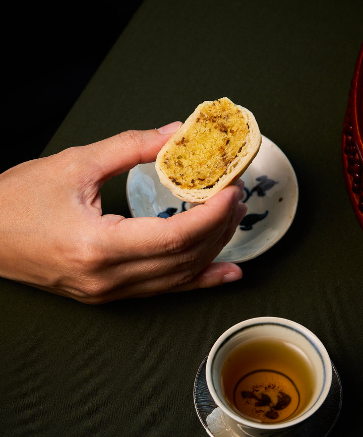 Person holding a half-eaten pastry with a cup of tea on a dark surface