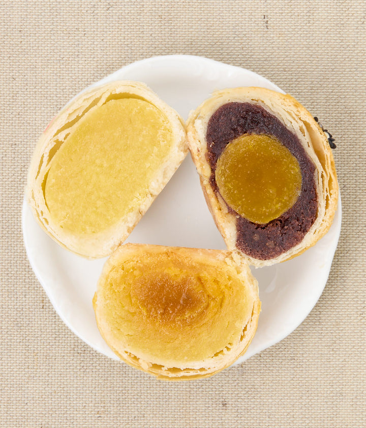 Three halved pastries on a white plate, showing yellow and dark brown fillings.