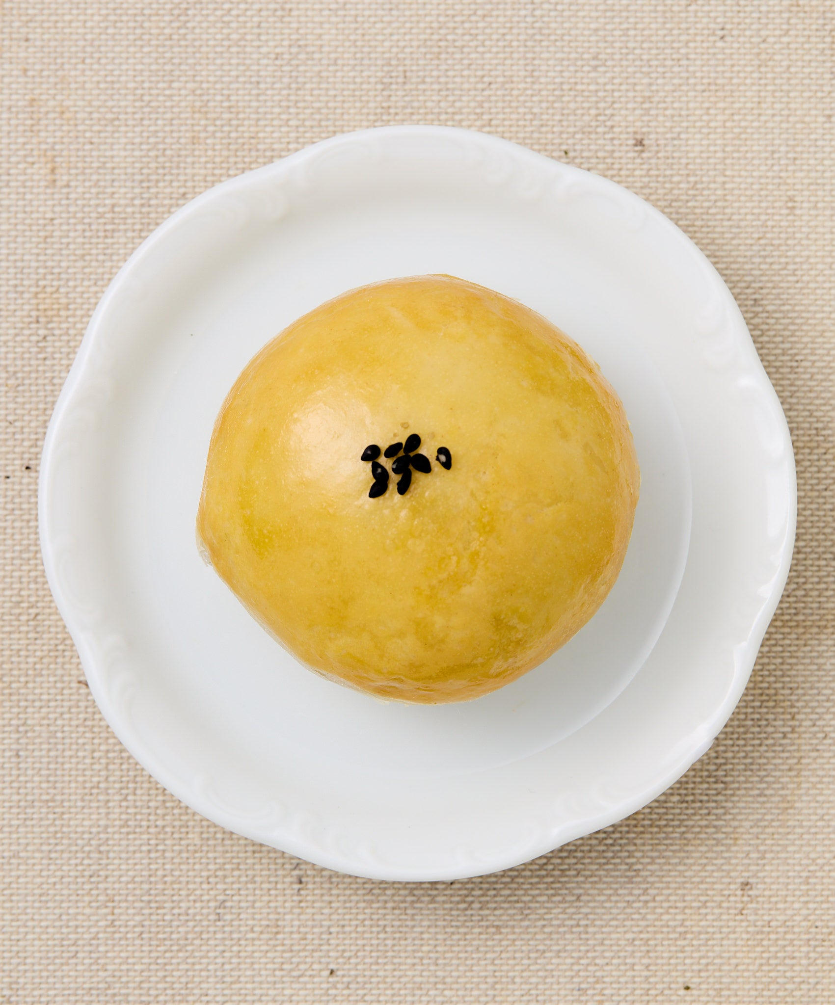 A whole Taiwanese mooncake with a golden, glossy surface topped with a few black sesame seeds, served on a white plate.