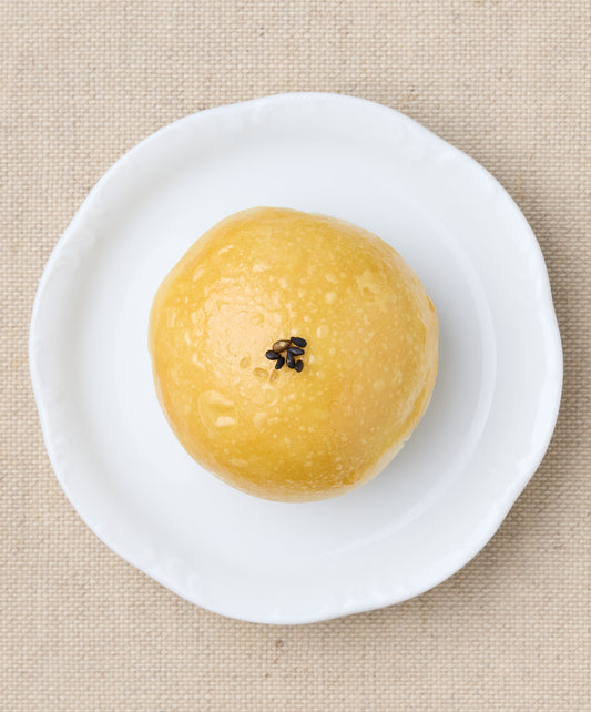 A whole Taiwanese mooncake with a golden, glossy surface topped with a few black sesame seeds, served on a white plate.