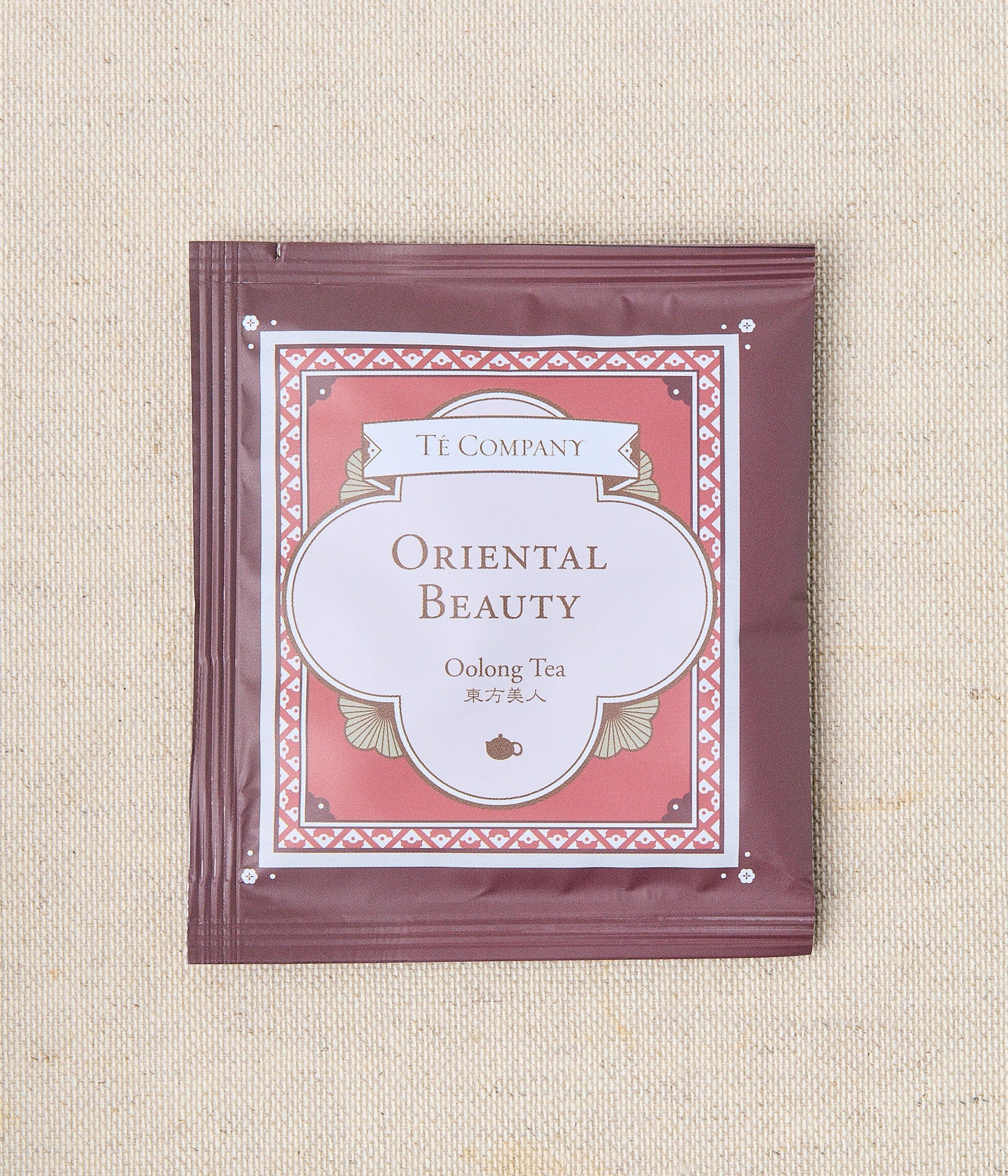 Single packet of Te Company Oriental Beauty oolong tea on a beige textured background.