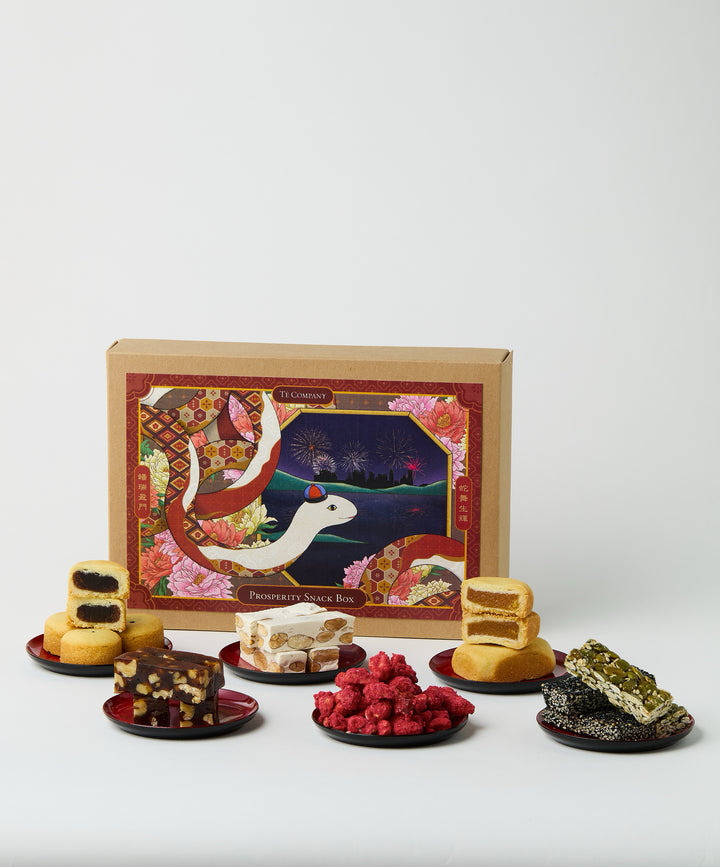 A display of Lunar New Year snacks from the Prosperity Snack Box, including traditional treats like nougats, pineapple cakes, and sesame bars, arranged with the festive packaging in the background.