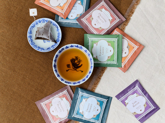 Cup of tea with assorted packaged tea sachets on a fabric surface.