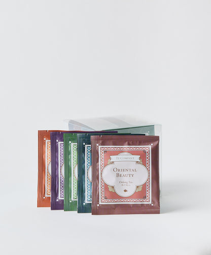 Five Te Company tea sachets arranged in a fan pattern, showing different colored packaging on a white background.